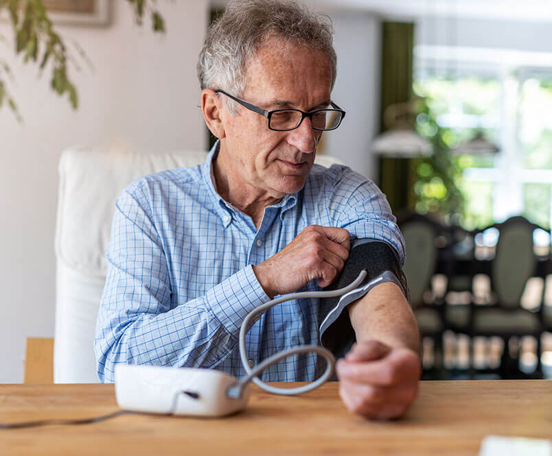 Sitting at a dining room table, man uses a device to check his blood pressure. Applying for Social Security Disability over 50 requires information about your age, background and medical status.
