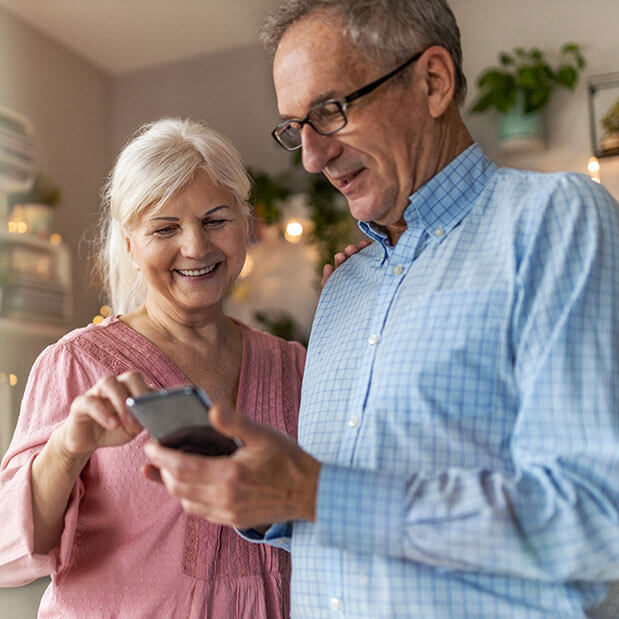 Standing next to each other and looking at a cell phone in his hand, a man and woman smile. The Clarkson Firm disability attorneys can answer questions about getting Social Security Disability benefits.