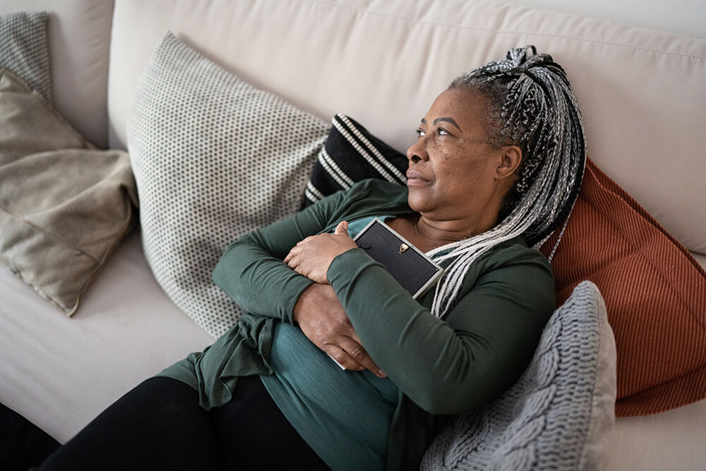 Reclining on a couch and looking to the side, a woman embraces a frame for a photo of a loved one. In the event of funeral home negligence, legal recourse is available to families.
