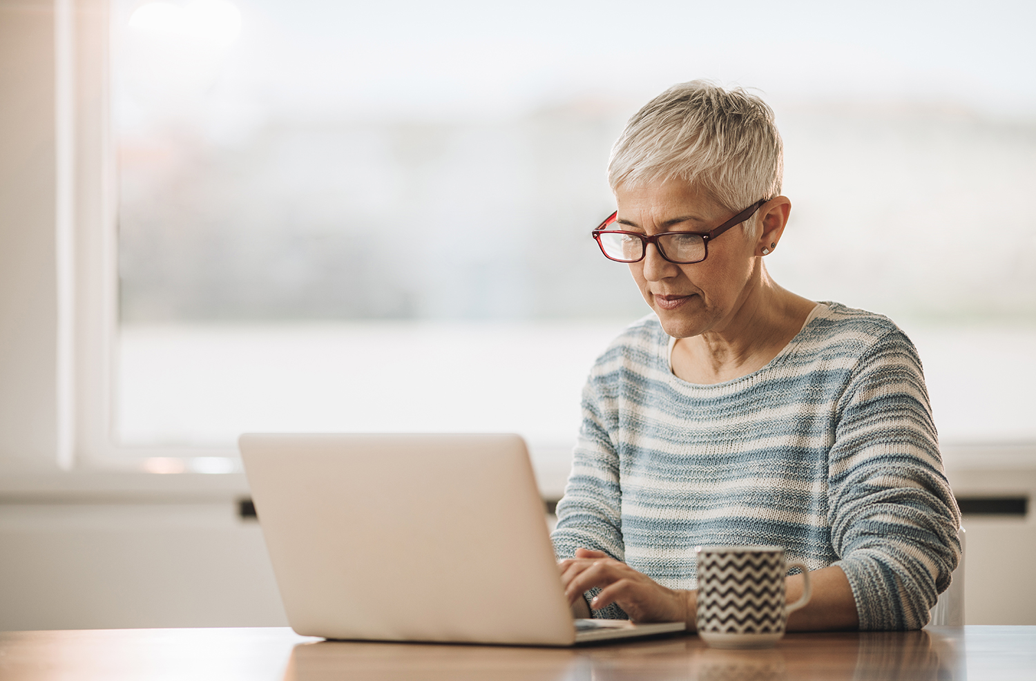 Coffee cup near at hand, a woman sits at a table and types on her laptop. The Alabama disability lawyer at The Clarkson Firm treats you like a person who deserves respect, not a case file.