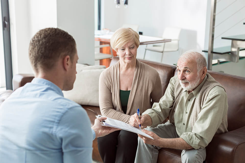 A man in professional dress holds out a clipboard while another man, seated next to a woman, holds a pen to the paper. You can qualify for Medicare health coverage along with disability benefits.