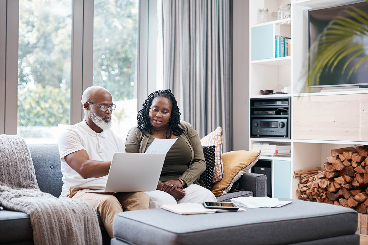 Sitting on a couch in their living room, a man and woman look over papers and a laptop. The Adult Function Report is a key form in the process of applying for disability benefits.