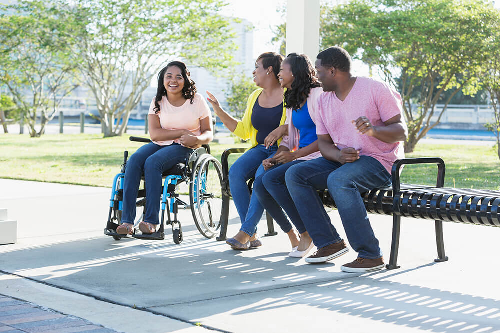 Three people sit on a park bench next to a woman in a wheelchair, all of them laughing and smiling. The Clarkson Firm disability attorneys can answer questions about getting Social Security Disability benefits.