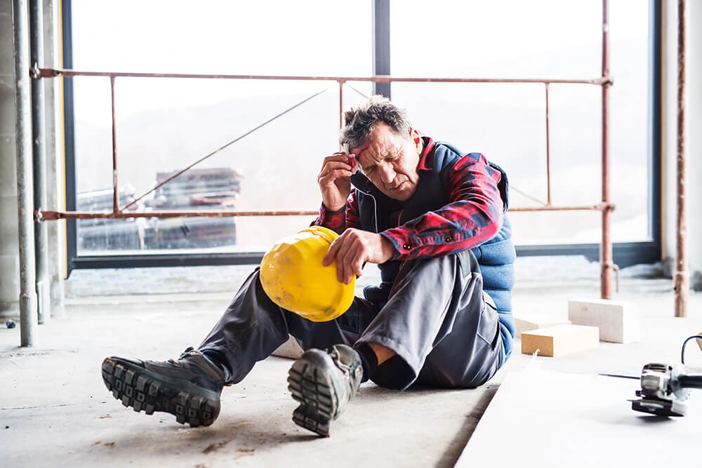 Sitting down in the middle of a construction site, a man holds his hardhat in one hand while dabbing an injury on his forehead with the other. You can only work a certain amount before Social Security will reject you for disability benefits.