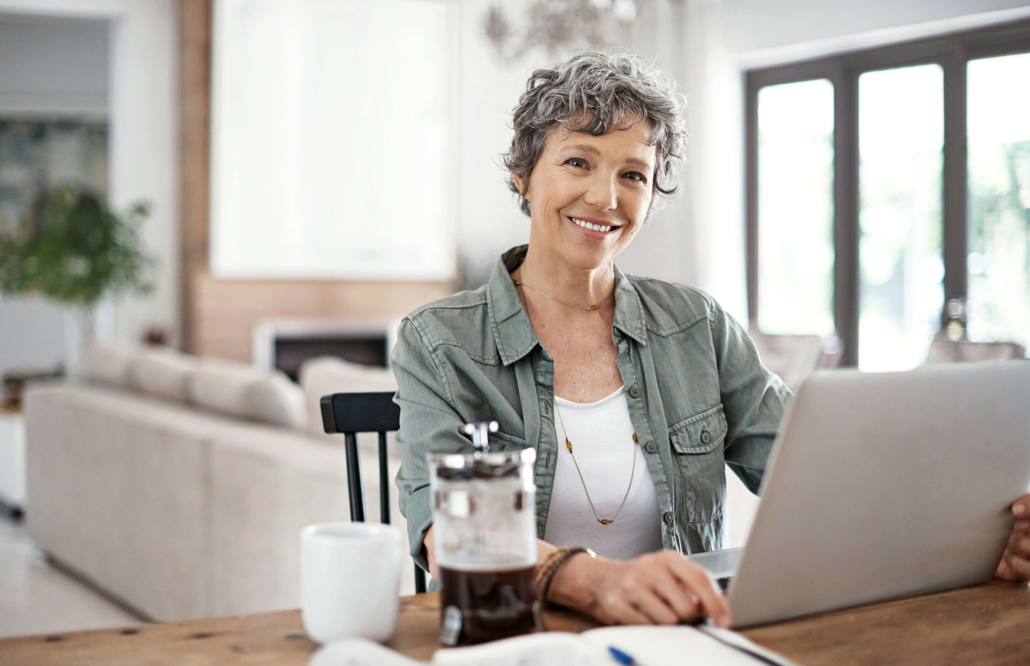 Sitting in front of her laptop at the dining room table, woman smiles. A disability lawyer can help you understand how to apply for Social Security Disability in Alabama.