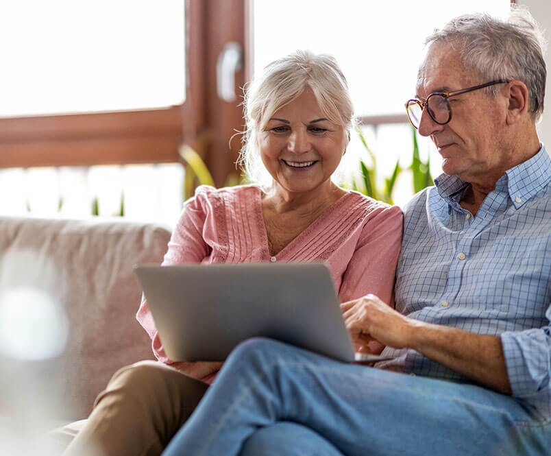 Sitting next to each other on a couch, a man and woman while looking at a laptop screen. Your age can make a difference in your Social Security Disability claim.