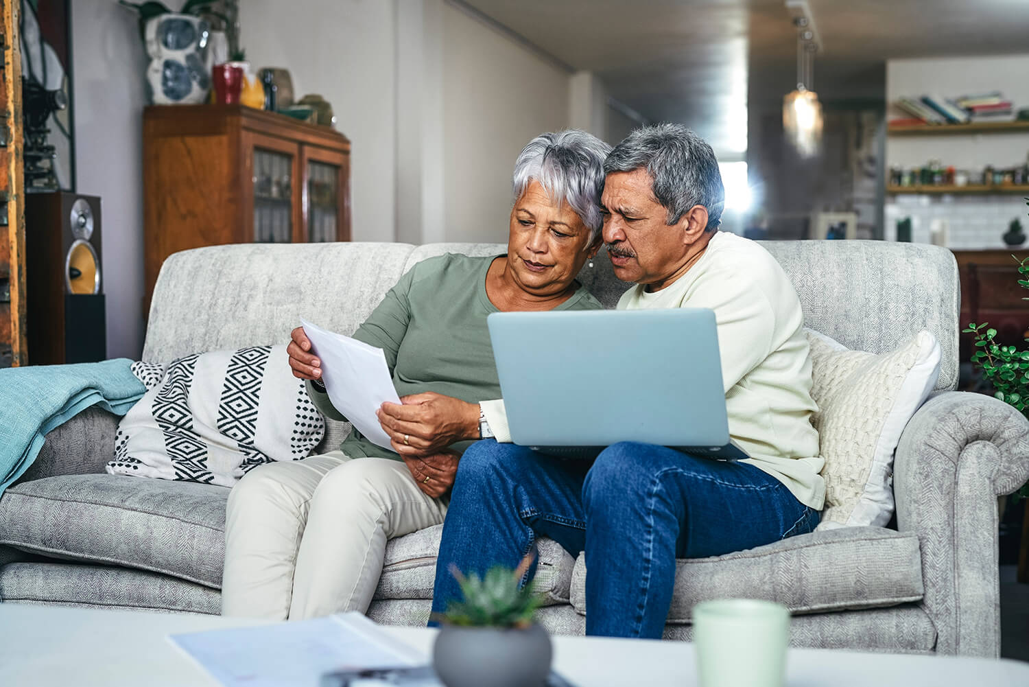 A man and woman sit on a couch going over paperwork with a laptop open. Applying for Social Security Disability benefits requires gathering a lot of information.